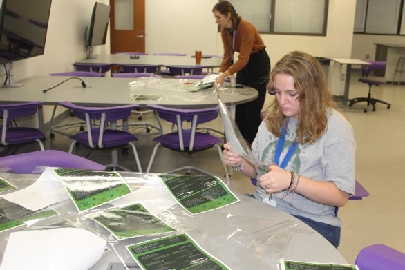Junior Gretchen Baron and sponsor Ms. Taylor Budzikowski cut out posters to hang around the school to raise awareness and help students know what to do in the event of a mental health crisis.