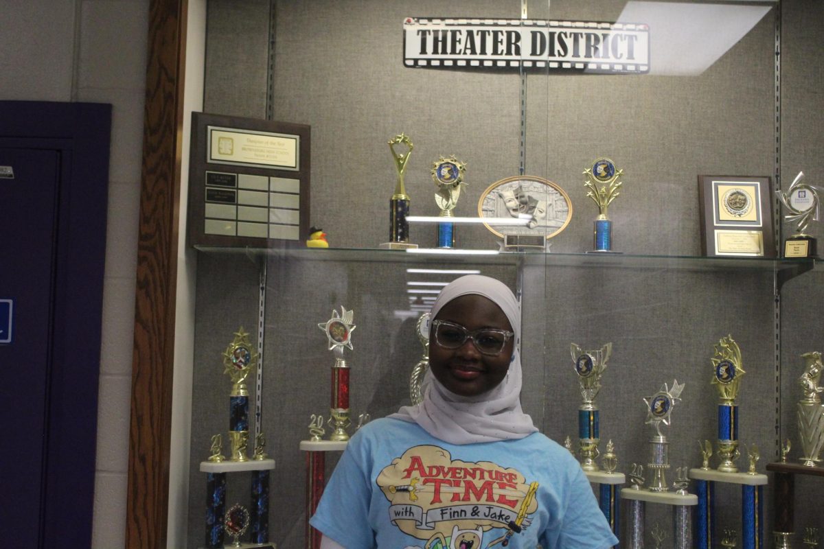 Lawal is standing in front of the theater trophy case. Lawal has participated in the productions in theater (“Shrek the Musical”, “Into the Woods” and “Peter and the Star Catcher”). Lawal hopes to continue her theater journey and participate in both acting and stage crew roles in the future.
